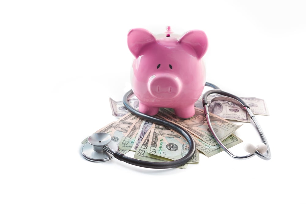 Piggy bank and stethoscope resting on pile of dollars on white background Piggy bank and stethoscope resting on pile of dollars on white background