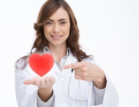 Pretty doctor holding and pointing at a red heart Pretty doctor holding and pointing at a red heart